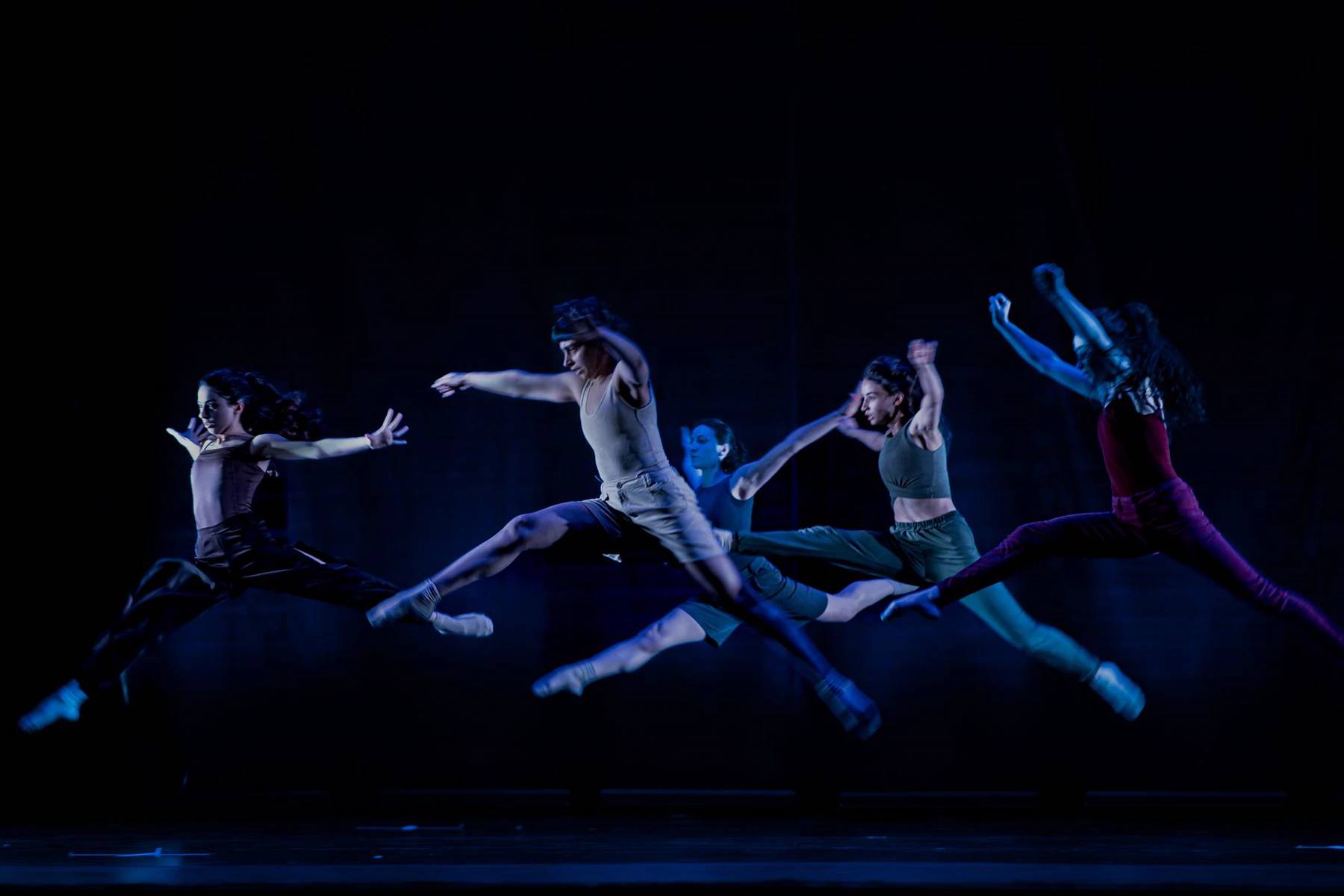 Professional dancers leaping across a dark stage under theatrical lights