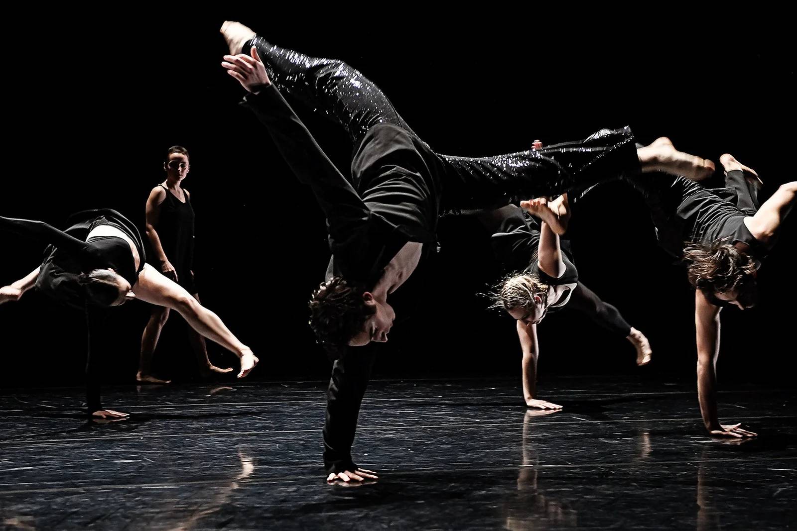 Contemporary dancers performing floorwork and handstand on a dark stage